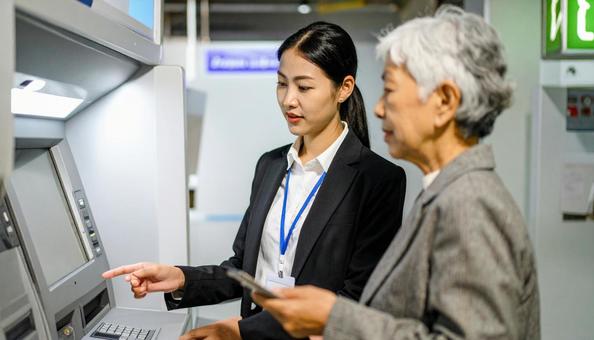 ATMでお金を引き出す老女と心配顔銀行員 ATMでお金を引き出す老女と心配顔銀行員の写真