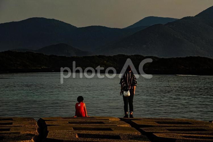 ＜素材＞堤防から夕暮れの海を眺める親子 家族,親子,女性の写真素材