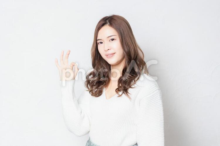 白い壁の前に立ってOKのジェスチャーをする若い女性 女性,ok,オッケーの写真素材