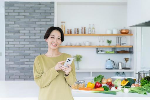 キッチンでスマホを持つミドルの女性 キッチンでスマホを持つミドルの女性 スマートフォン,キッチン,台所の写真素材
