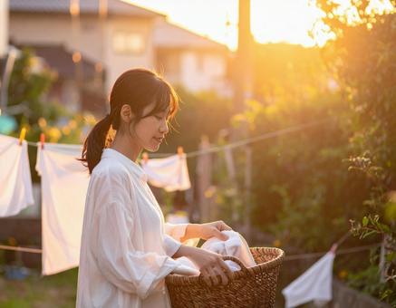 夕暮れ時に洗濯物を取り込む女性 夕暮れ時に洗濯物を取り込む女性の写真