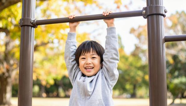 公園の鉄棒にぶら下がって笑顔の男の子 公園の鉄棒にぶら下がって笑顔の男の子の写真