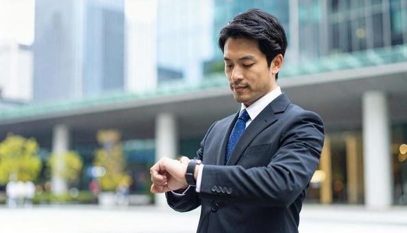 腕時計を見るビジネスマン 街中 腕時計を見るビジネスマン 街中の写真