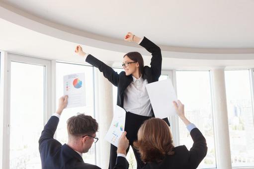 窓の外を見るメガネの女性と書類を持つ男性の後ろ姿の写真