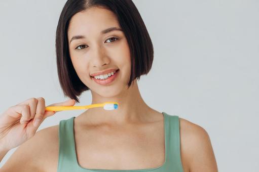 黄色の歯ブラシを持ってブラシ面を見せる女性 黄色の歯ブラシを持ってブラシ面を見せる女性の写真