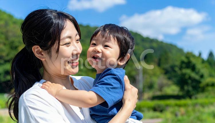 青空の下、子供を抱っこする母親 親子,母親,母子の写真素材