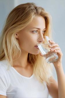 コップの水を飲む金髪の外国人女性の写真