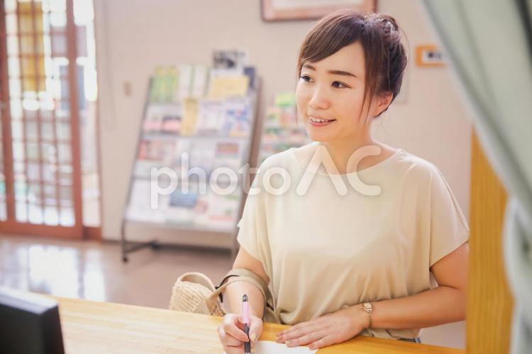 受付で何か書き込む女性 受付,チェックイン,カウンターの写真素材