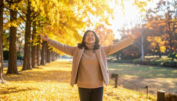 秋の紅葉を楽しみながら公園を散歩する女性 秋の紅葉を楽しみながら公園を散歩する女性の写真