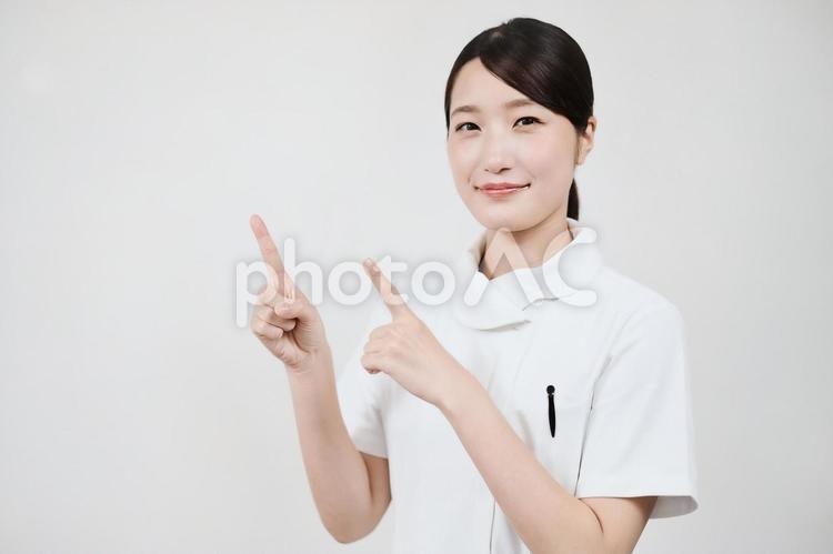 指さしのポーズをする白衣の女性  看護師,ナース,女性の写真素材