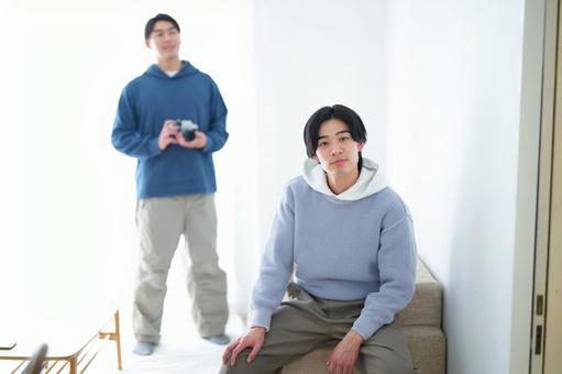 ソファの肘掛けに座っている男性とカメラを持って立っている男性 ソファの肘掛けに座っている男性とカメラを持って立っている男性 引っ越し,一人暮らし,男性の写真素材