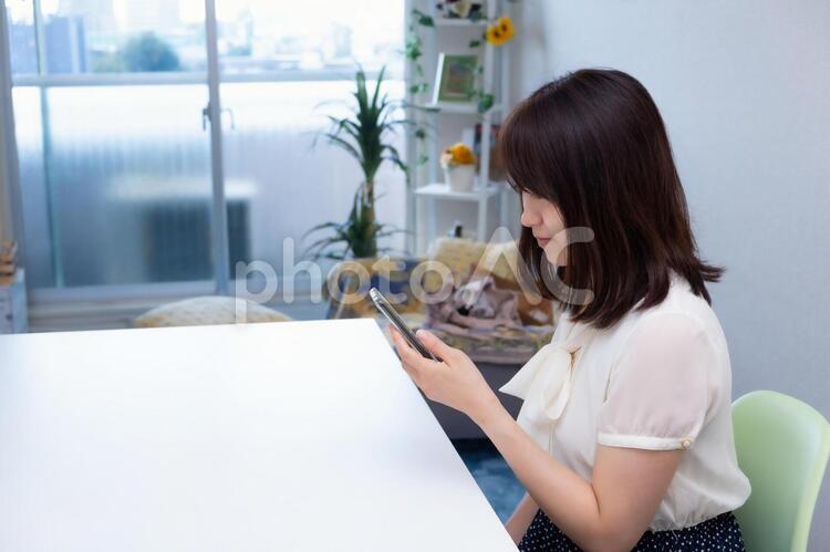 室内で椅子に座りスマホを操作する女性 女性,スマートフォン,スマホの写真素材