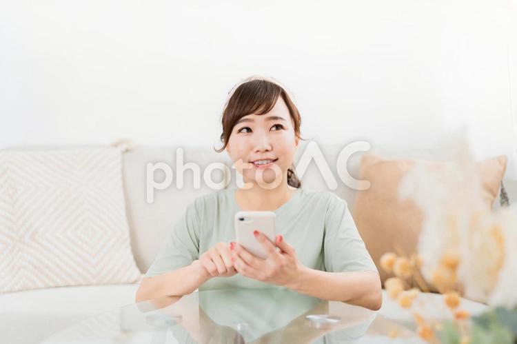 家でスマホを使う笑顔の日本人女性 スマホ,考える,迷うの写真素材