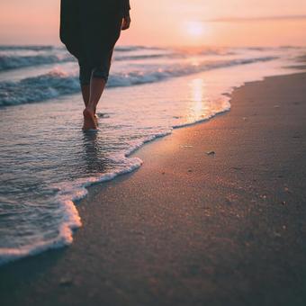 夕日に輝くビーチを歩く女性の足元の写真