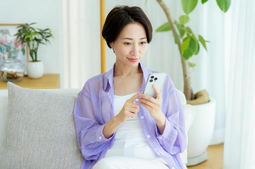 部屋でスマホを使うミドル女性 スマホ,笑顔,女性の写真素材