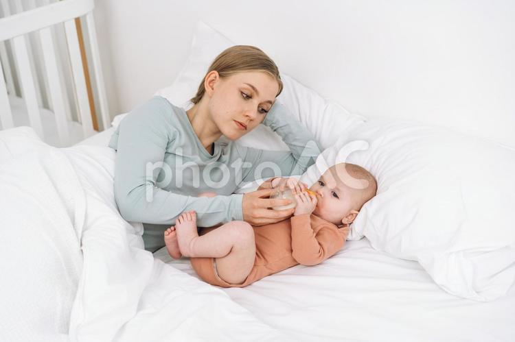 ベッドでミルクを飲んでいる赤ちゃんを見ている母 親子,赤ちゃん,哺乳瓶の写真素材