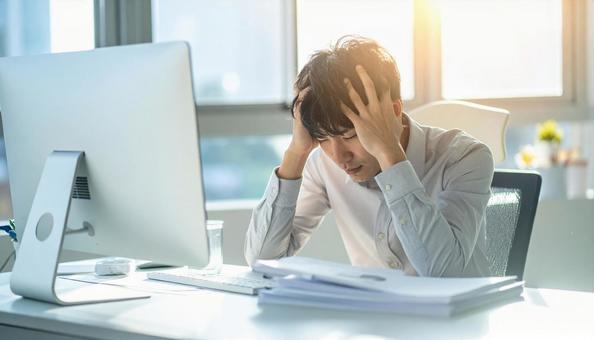 デスクで頭を抱えているビジネスマンの写真