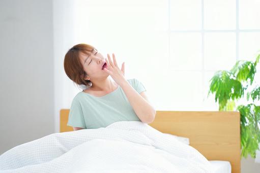 口に手を当てあくびする女性の写真