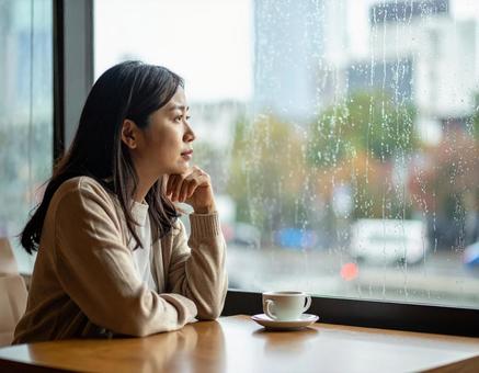 雨の日にカフェで外を見つめる女性の写真