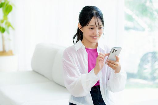 部屋でスマホを操作する若い女性 スマホ,若い女性,笑顔の写真素材