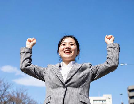青空の下ガッツポーズする女性社員 青空の下ガッツポーズする女性社員の写真