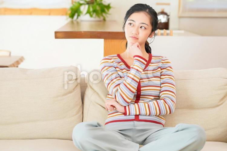 ソファーにあぐらで座って考える女性 女性,主婦,休日の写真素材