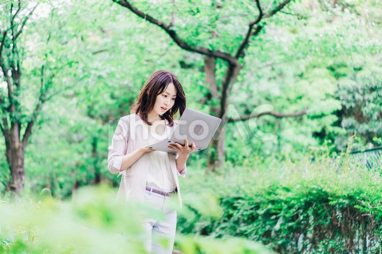 外でパソコンを使う若いビジネスウーマン 白背景,ビジネス,働くの写真素材