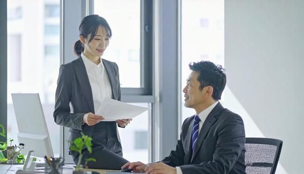 上司に報告する女性社員の写真