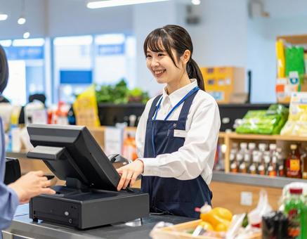 スーパーで笑顔でレジ業務をする女性店員 スーパーで笑顔でレジ業務をする女性店員の写真