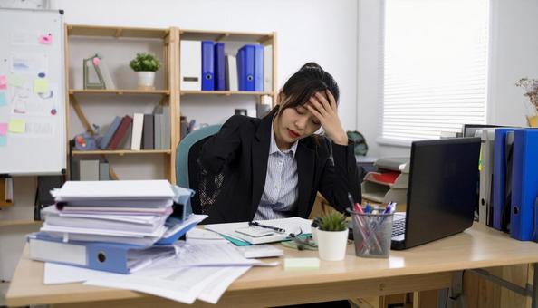デスクに仕事の書類が山積みになる女性 デスクに仕事の書類が山積みになる女性の写真