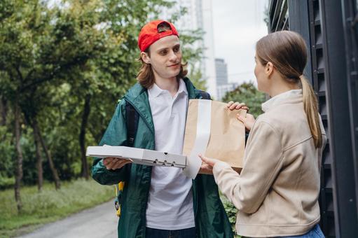 家の門の前でフードデリバリーを受け取る女性 配達,フードデリバリー,デリバリーの写真素材