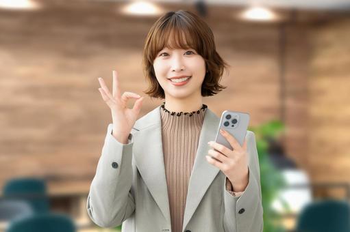 スマホを持ってOKポーズをする笑顔の女性 女性,ok,スマホの写真素材