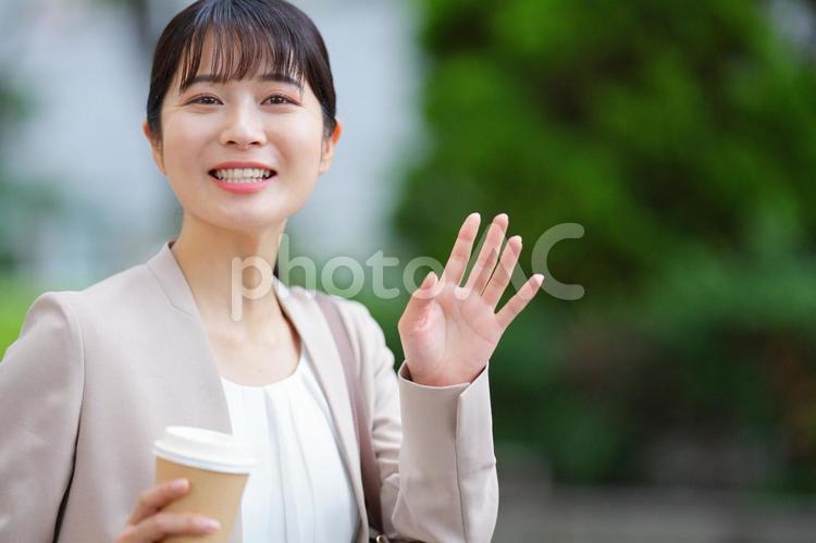 カメラ目線でコーヒーを持って手を振る女性 女性,人物,大学生の写真素材