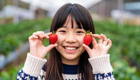 苺狩りで苺を両ほほに掲げる可愛い女の子 苺狩りで苺を両ほほに掲げる可愛い女の子の写真