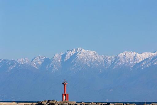 海と雪山の絶景｜赤い灯台の写真