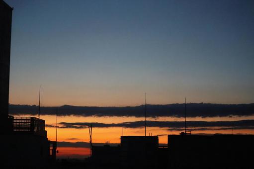 オレンジ色の夕空と黒いシルエットの街並みの写真