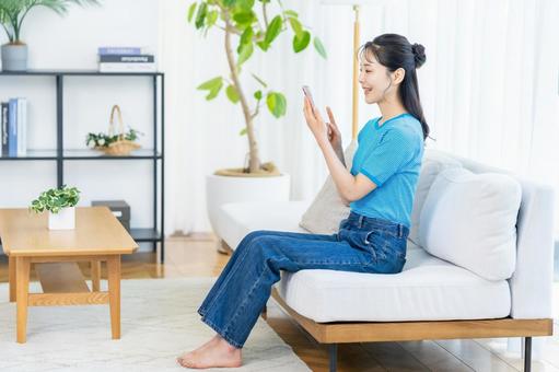 部屋でスマホを操作する女性 スマホ,笑顔,部屋の写真素材