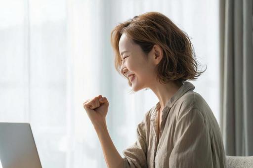 PC前で笑顔のガッツポーズ女性 PC前で笑顔のガッツポーズ女性の写真