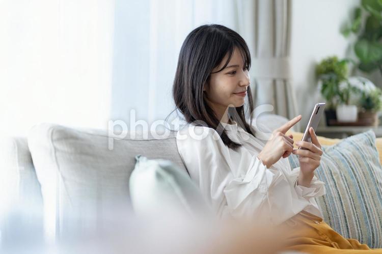 ソファで携帯を持つ日本人女性 スマホ,スマートフォン,操作の写真素材