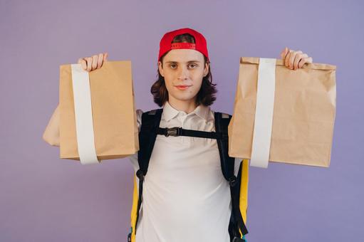 紙袋を２個持つフードデリバリーの男性の写真