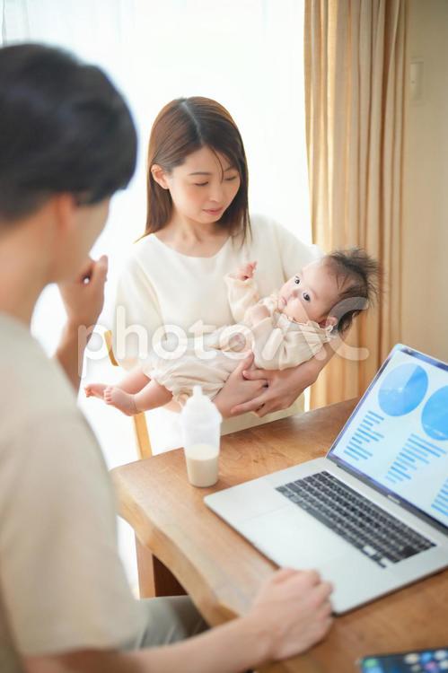 ダイニングでノートパソコンを使うお父さんと赤ちゃんを抱っこしているお母さん 家族,親子,お父さんの写真素材