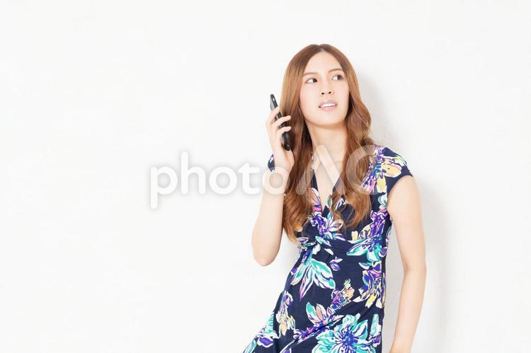 白い壁の前で、スマホを使う、青いワンピースを着た若い女性 女性,スマホ,携帯電話の写真素材