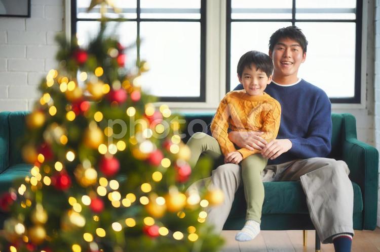 ソファーに座って男性の膝に抱っこされる男の子とクリスマスツリー 親子,男の子,小学生の写真素材