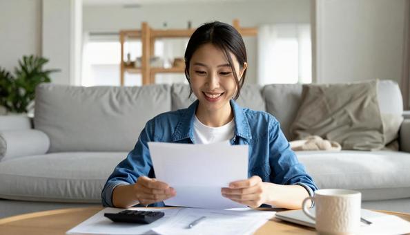 リビングで通帳を笑顔で確認する女性 リビングで通帳を笑顔で確認する女性の写真