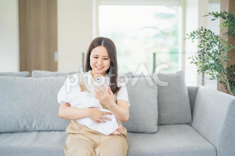 赤ちゃんを抱きながらスマホを使う女性 赤ちゃん,ママ,子育ての写真素材