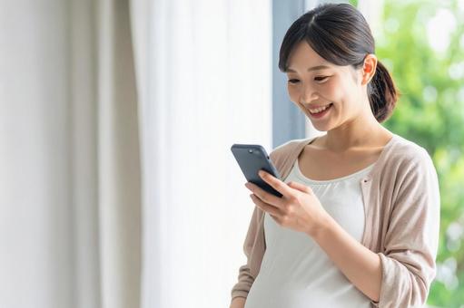 スマホを操作する若い日本人の妊婦 スマホを操作する若い日本人の妊婦の写真