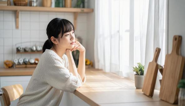 疲れた表情でキッチンに座る若い女性 疲れた表情でキッチンに座る若い女性の写真