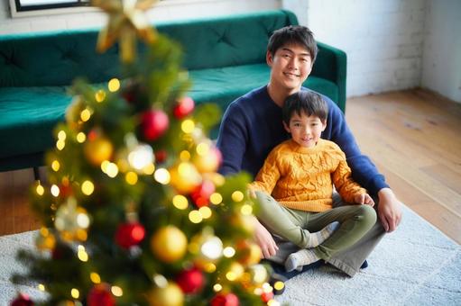 絨毯にあぐらで座る親子と横にクリスマスツリー 絨毯にあぐらで座る親子と横にクリスマスツリーの写真