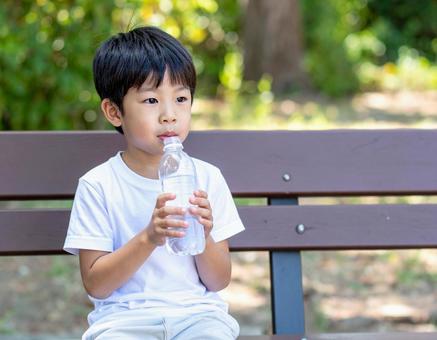 公園のベンチで水を飲む少年 公園のベンチで水を飲む少年の写真