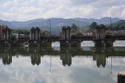 洗堰の水門と山と空のうつる水面の川の風景の写真